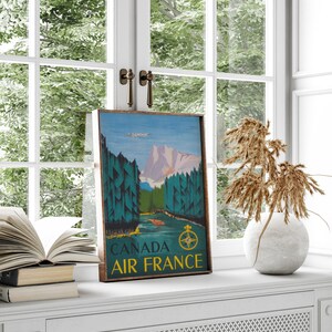 May include: A vintage travel poster for Air France featuring a scenic landscape with mountains, trees, and a river. The poster is framed in wood and has the text "CANADA AIR FRANCE" at the bottom.