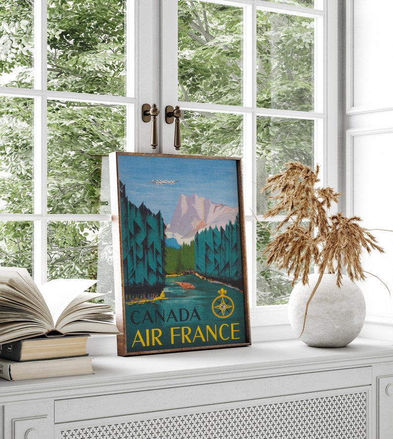 May include: A vintage travel poster for Air France featuring a scenic landscape with mountains, trees, and a river. The poster is framed in wood and has the text "CANADA AIR FRANCE" at the bottom.
