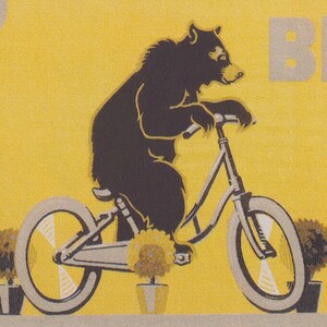 Op de afbeelding: Een zwarte beer fietst op een gele achtergrond. De fiets is grijs en heeft grote wielen. Twee potplanten en een zonnebloem staan bij de fiets. Het woord "BE" is zichtbaar op de achtergrond.