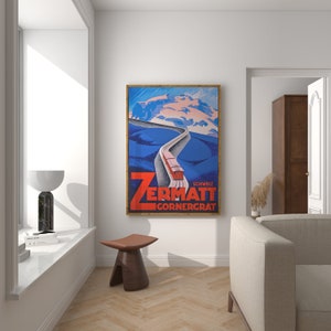 May include: A framed vintage travel poster for Zermatt, Switzerland, featuring a red train ascending a winding road towards snow-capped mountains. The poster has a blue and white color scheme with the text "Zermatt Gornergrat" in bold red letters.
