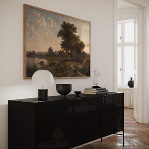 K&ouml;nnte beinhalten: Ein schwarzer Metallschrank mit einer Drahtgitterfront, eine wei&szlig;e Lampe mit einem wei&szlig;en Schirm, eine schwarze Schale und eine wei&szlig;e Skulptur darauf. Der Schrank steht vor einer wei&szlig;en Wand mit einem gerahmten Landschaftsbild.