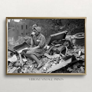 May include: Black and white framed print featuring a woman in a headscarf drinking from a cup, seated amidst rubble. The print has a gold frame and the text "VIBRANT VINTAGE PRINTS" at the bottom.