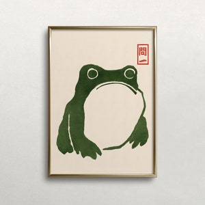 Puede incluir: Una impresión enmarcada de una rana verde con un diseño simple y minimalista. La rana está delineada en negro y tiene un fondo blanco. La impresión está enmarcada en un marco dorado y tiene un sello rojo con caracteres japoneses en la esquina superior derecha.