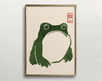 May include: A framed print of a green frog with a simple, minimalist design. The frog is outlined in black and has a white background. The print is framed in a gold frame and has a red seal with Japanese characters in the top right corner.