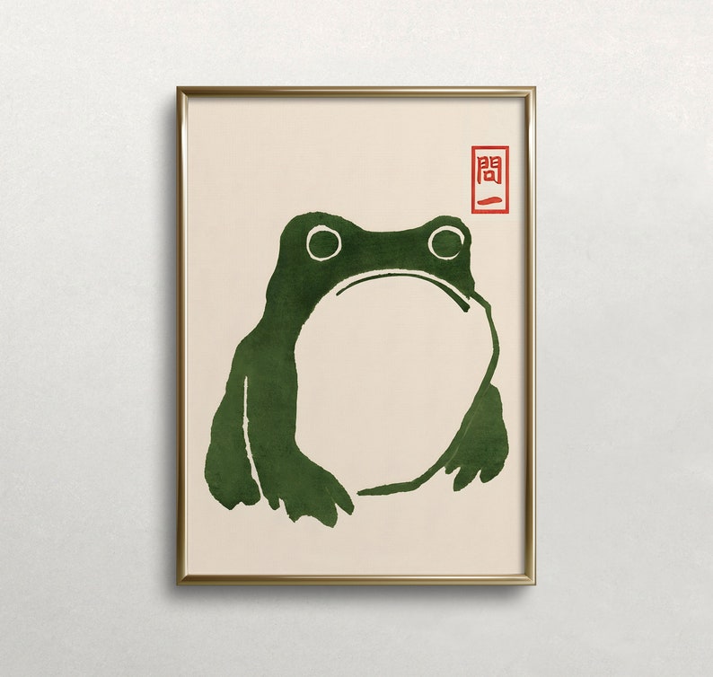 May include: A framed print of a green frog with a simple, minimalist design. The frog is outlined in black and has a white background. The print is framed in a gold frame and has a red seal with Japanese characters in the top right corner.