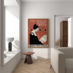 May include: A framed vintage poster for The Boston Sunday Herald, featuring a woman in a black dress reading. The poster has a red background with floral accents and the text "Ladies Want it Feb 24".