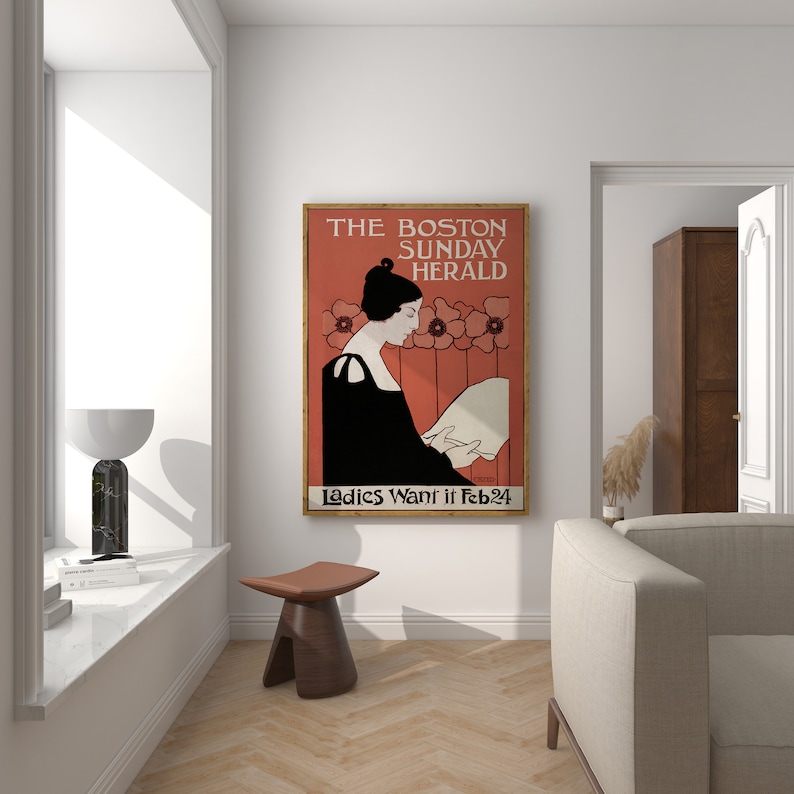 May include: A framed vintage poster for The Boston Sunday Herald, featuring a woman in a black dress reading. The poster has a red background with floral accents and the text "Ladies Want it Feb 24".