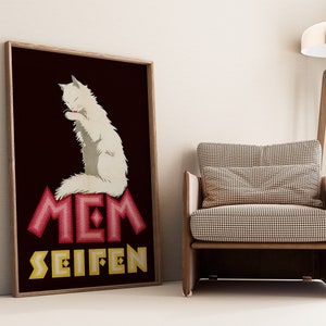 May include: Framed vintage poster featuring a white cat grooming itself, set against a dark maroon background. The poster has the words "MEM SEIFEN" in red and yellow. The poster is displayed next to a wooden chair.