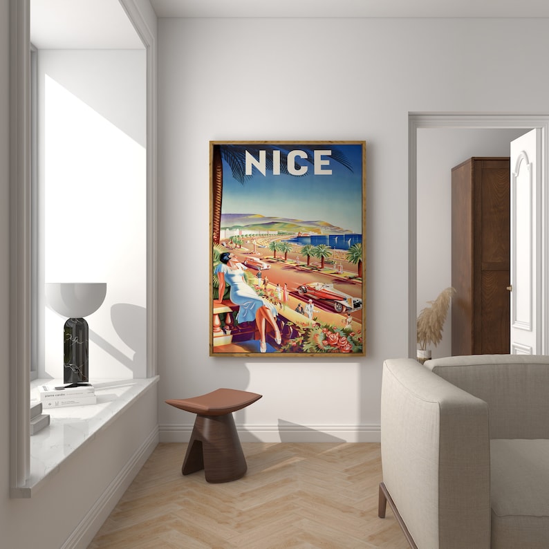 Puede incluir: Un p&oacute;ster de viaje vintage enmarcado con la palabra "NICE" en la parte superior. El p&oacute;ster representa a una mujer con un vestido azul claro, palmeras, coches cl&aacute;sicos y una escena costera. El p&oacute;ster se exhibe en una pared blanca.