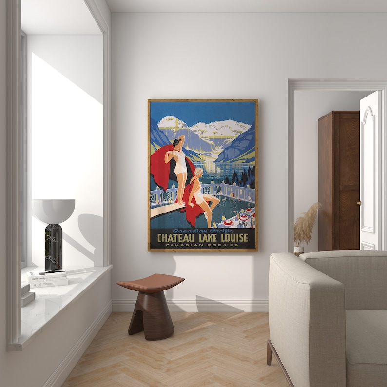 May include: Vintage travel poster advertising Chateau Lake Louise in the Canadian Rockies. The poster features two women in swimsuits standing on a diving board overlooking a lake with mountains in the background. The poster is framed in a wooden frame.