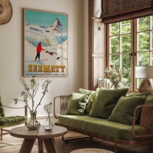 Puede incluir: Un sof&aacute; de terciopelo verde con un marco de mimbre se encuentra en una sala de estar con un cartel de esqu&iacute; vintage que dice "Zermatt Suiza". El cartel presenta a un esquiador con una chaqueta roja y una cordillera en el fondo.