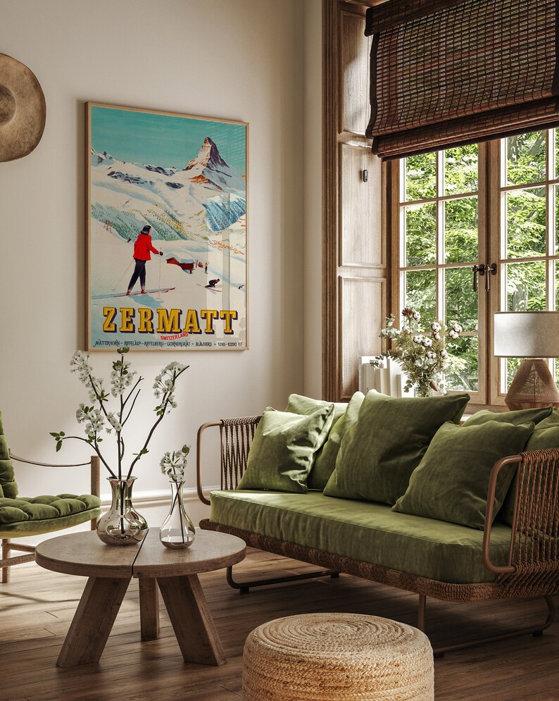 Puede incluir: Un sof&aacute; de terciopelo verde con un marco de mimbre se encuentra en una sala de estar con un cartel de esqu&iacute; vintage que dice "Zermatt Suiza". El cartel presenta a un esquiador con una chaqueta roja y una cordillera en el fondo.