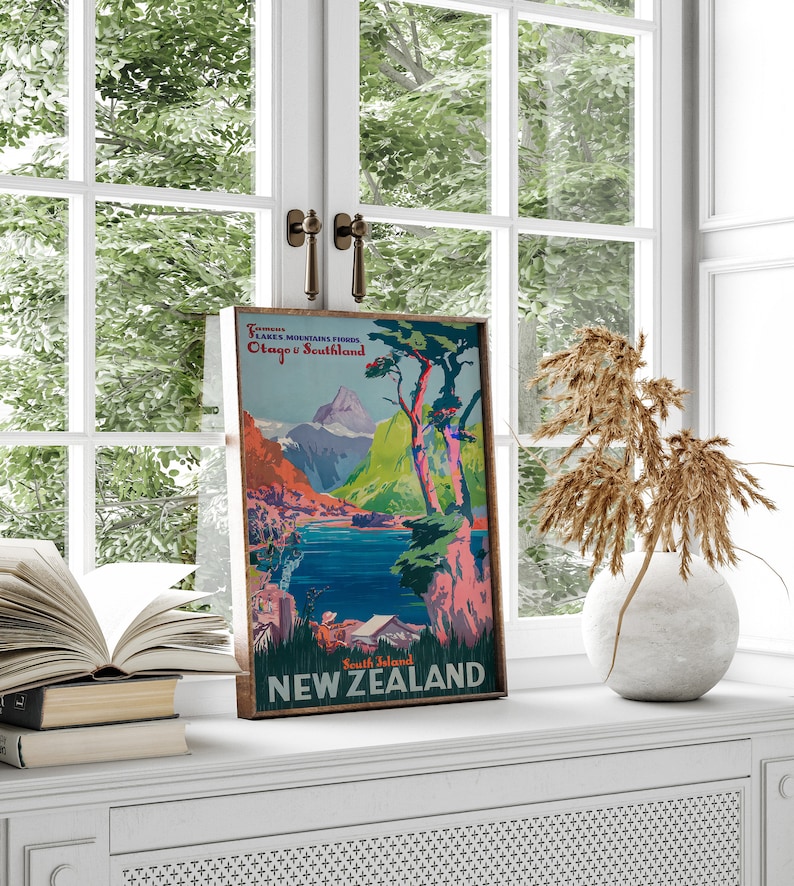 May include: Vintage travel poster featuring a scenic view of mountains, a lake, and trees. The poster is titled "New Zealand" and includes the text "Tourist Lakes Mountains Fiords Otago & Southland South Island".