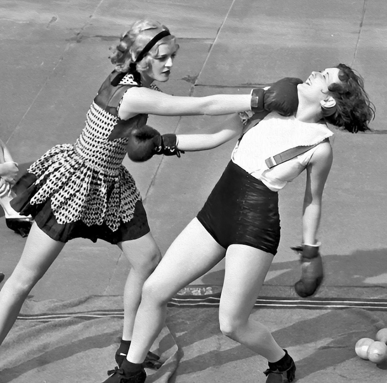 Puede incluir: Fotograf&iacute;a en blanco y negro de dos mujeres boxeando. Una, con un vestido de lunares y guantes de boxeo, lanza un pu&ntilde;etazo. La otra, con una camiseta blanca y pantalones cortos negros, es golpeada. Ambas llevan guantes de boxeo.