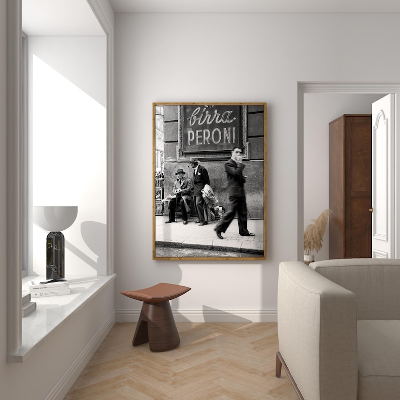 Pu&ograve; includere: Stampa incorniciata in bianco e nero raffigurante una scena di strada con la scritta "birra PERONI". L'immagine mostra tre uomini, uno che cammina e due seduti, di fronte a un edificio. La stampa &egrave; esposta in una stanza dall'estetica moderna.