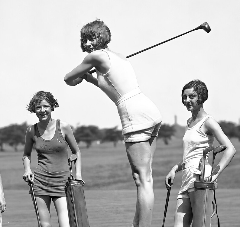 May include: Three women on a golf course, two holding golf clubs and one holding a golf bag. The woman in the center is wearing a white tank top and white shorts. The woman on the left is wearing a red tank top and the woman on the right is wearing a white tank top and white shorts.