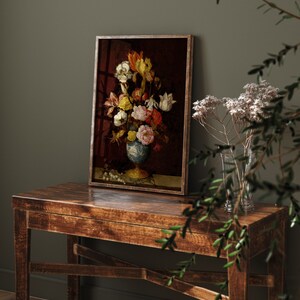May include: A framed floral still life painting featuring a vase filled with colorful flowers. The vase is blue and white, set against a dark red background. The painting is displayed on a rustic wooden table.