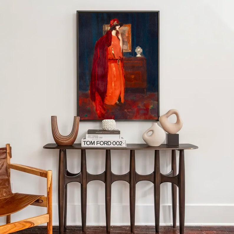 May include: A dark wood console table with a unique, modern design. The table has four legs with a curved shape and a rectangular top. The table is decorated with a white ceramic sculpture, a stack of books, and a ceramic vase. A framed painting of a woman in a red dress hangs on the wall behind the table.