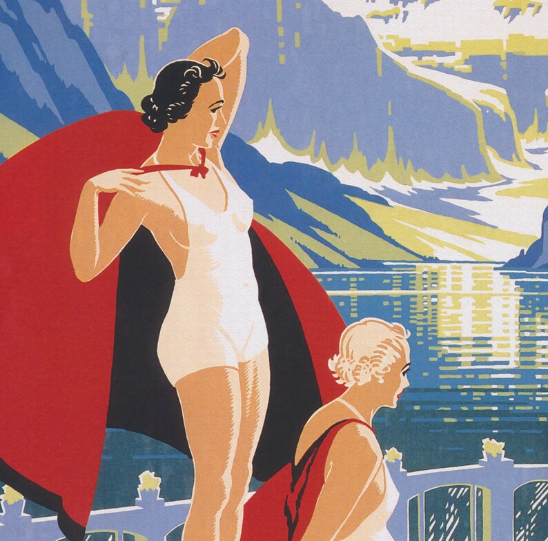 May include: Two women in vintage swimwear stand in front of a mountain lake. One woman wears a white swimsuit and a red cape. The other woman wears a white swimsuit and a red and black cape. The lake is blue and the mountains are green and white.