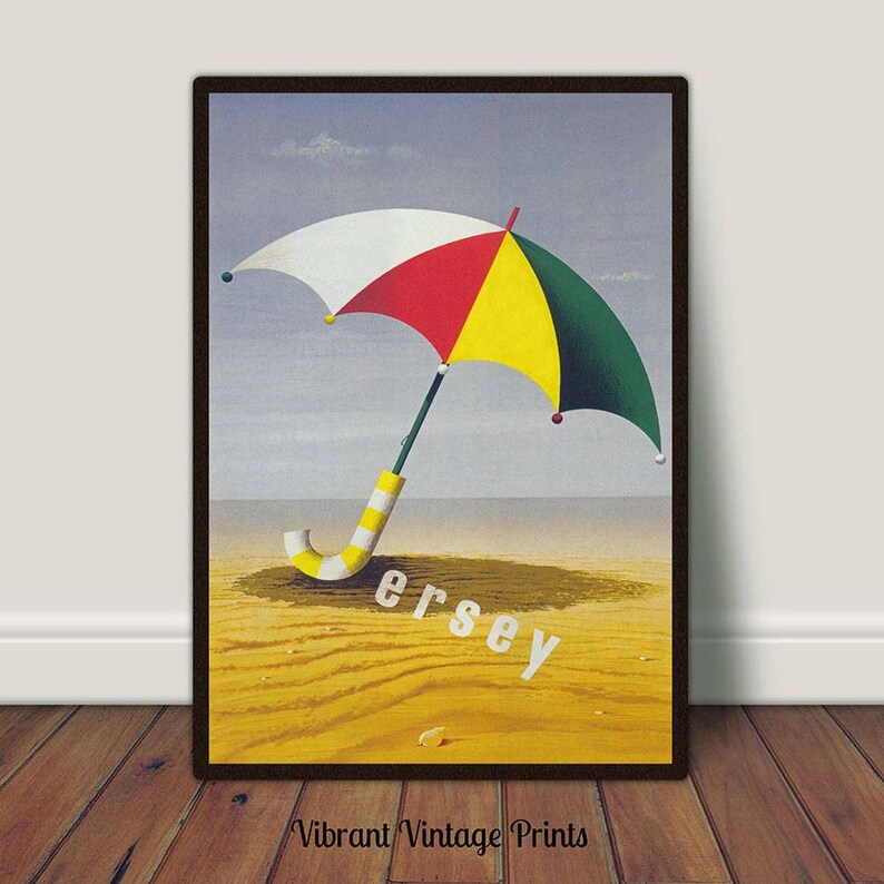 May include: Framed print of a colourful umbrella on a sandy beach. The umbrella has white, red, yellow, and green panels. The word "Jersey" is printed in white. The print is set against a light blue sky and a brown frame.