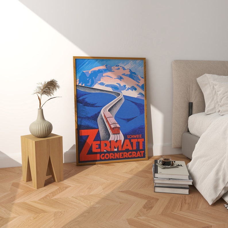 May include: A framed vintage travel poster for Zermatt, Switzerland, featuring a red train on a winding track against a blue and white mountain backdrop. The poster has a wooden frame and is displayed near a bed and a wooden side table.