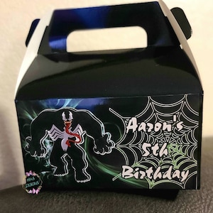 May include: Black and green favor box with a cartoon image of Venom, a Marvel Comics character. The box has a white handle and says "Aaaron's 5th Birthday" on the front.