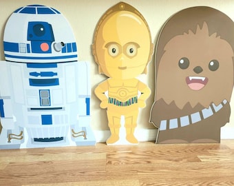 May include: Three cardboard cutouts of Star Wars characters: R2-D2, C-3PO, and Chewbacca. The characters are depicted in a cartoon style with bright colors and simple features.