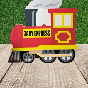 May include: A red and yellow toy train with black wheels and a white smoke plume. The train has a yellow window and a sign that reads "ZANY EXPRESS".