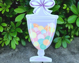 May include: A purple glass candy jar with a purple bow on top. The jar is filled with colorful swirl candies.