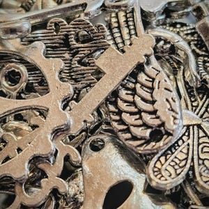 May include: A close-up of a collection of silver-colored charms. The charms include keys, gears, and other decorative shapes. The charms are clustered together, creating a textured and detailed appearance.