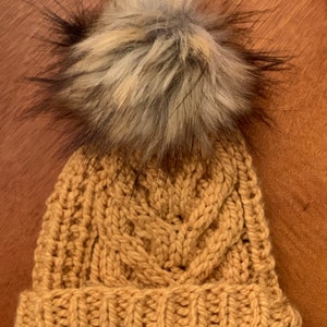 May include: A mustard yellow knitted beanie with a large black and white faux fur pom pom.