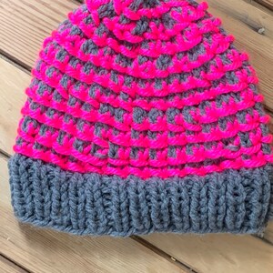 May include: A gray and pink knitted beanie hat. The hat has a gray brim and a pink and gray patterned crown.