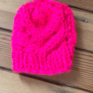 May include: A bright pink knitted hat with a cable knit pattern.