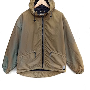 Op de afbeelding: Een bruine capuchontrui met een ritssluiting en een zwart logo-patch met de tekst "Killer Loop" aan de rechteronderkant.