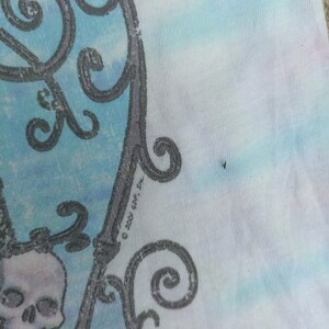 May include: A tie-dye t-shirt with a skull and decorative ironwork design. The design is in grey and white, set against a backdrop of blue, white, and pink tie-dye. The text "&copy; 2001 GDP, Inc." is visible.