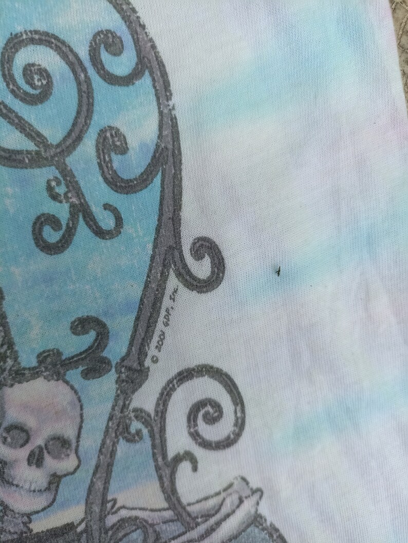 May include: A tie-dye t-shirt with a skull and decorative ironwork design. The design is in grey and white, set against a backdrop of blue, white, and pink tie-dye. The text "&copy; 2001 GDP, Inc." is visible.