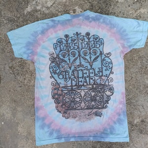 May include: Tie-dye t-shirt with a graphic featuring a gate design, skeletons, and the text "Grateful Dead" and the years "1965 1995". The shirt has a blue, purple, and white spiral pattern.