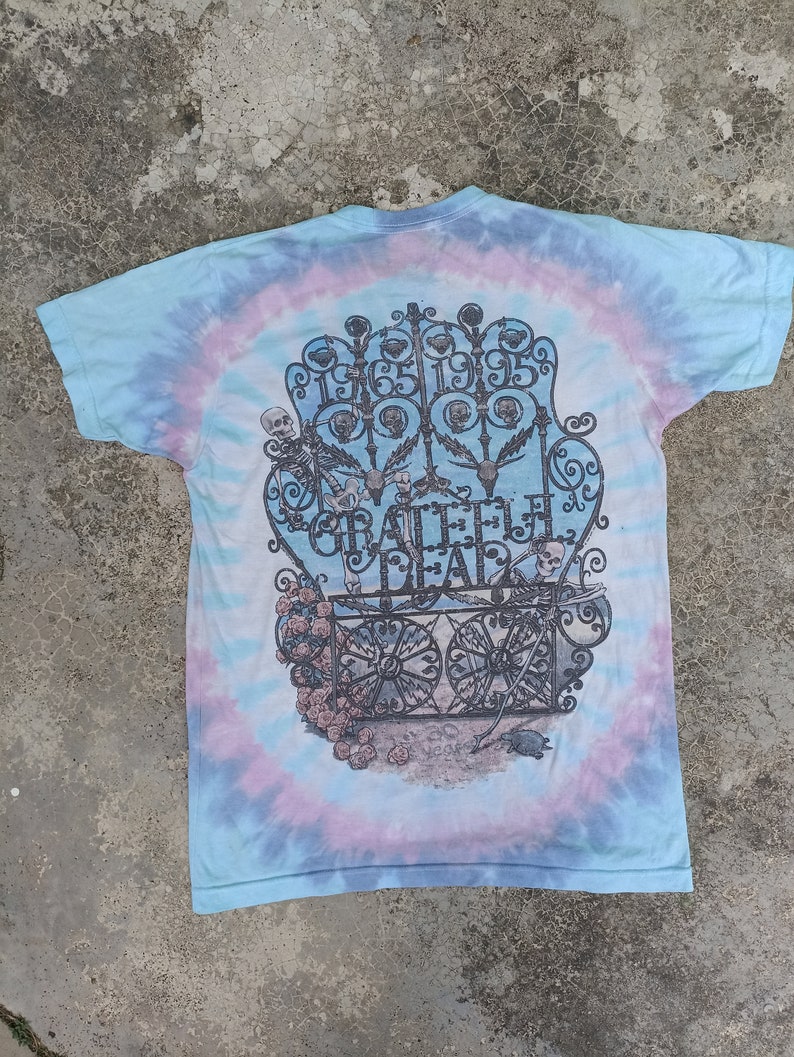 May include: Tie-dye t-shirt with a graphic featuring a gate design, skeletons, and the text "Grateful Dead" and the years "1965 1995". The shirt has a blue, purple, and white spiral pattern.