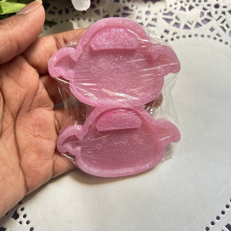 May include: Two pink silicone molds in the shape of a teapot. The molds are packaged in clear plastic wrap.