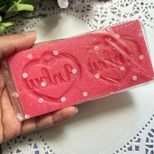 May include: Pink silicone mold with white polka dots. The mold has two heart shapes with the words "mama" and "dada" inside.