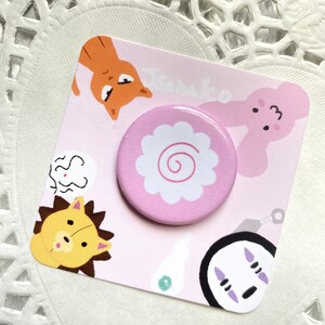 May include: A pink and white button with a swirl design. The button is on a card with illustrations of a cat, a rabbit, a lion, and a No Face character from the movie Spirited Away.