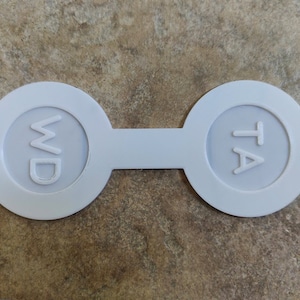 May include: White plastic tag with two circles. The left circle has the letters "WD" inside and the right circle has the letters "TA" inside.