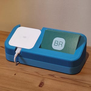 May include: A blue business card holder with a white square device and a stack of green cards. The cards have the letters "BR" in a white circle. The device has a white cord attached.