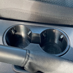 May include: Close-up of a black car cup holder with two empty cup slots.