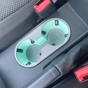 May include: A close-up of a car's center console with two cup holders. The cup holders are made of gray plastic and have a light blue liner. The cup holders are empty.