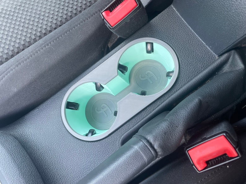May include: A close-up of a car's center console with two cup holders. The cup holders are made of gray plastic and have a light blue liner. The cup holders are empty.