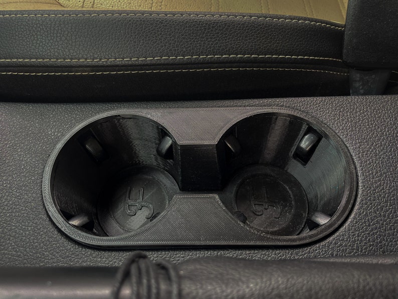 May include: Close-up of a black plastic cup holder with two circular openings. The cup holder is mounted in a black leather surface.