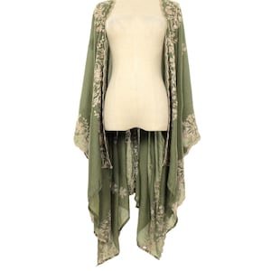May include: Olive green kimono-style cover-up with floral embroidery. The open-front design features long sleeves and a flowing, asymmetrical hemline. The embroidery is in a contrasting light beige color, adding a delicate touch to the garment. The cover-up is displayed on a mannequin.
