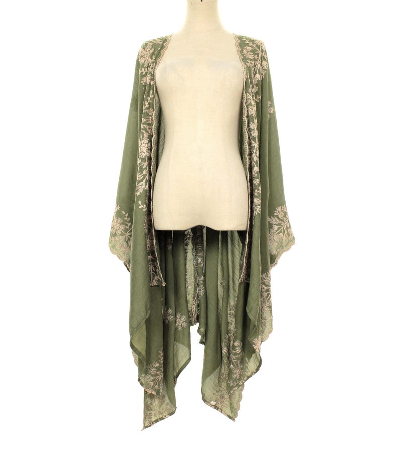 May include: Olive green kimono-style cover-up with floral embroidery. The open-front design features long sleeves and a flowing, asymmetrical hemline. The embroidery is in a contrasting light beige color, adding a delicate touch to the garment. The cover-up is displayed on a mannequin.
