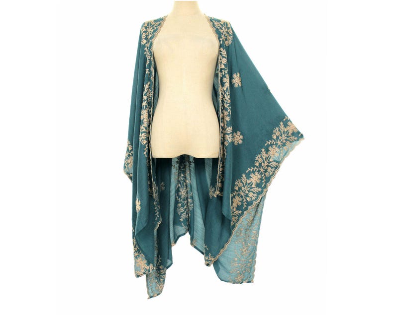 May include: Teal-colored embroidered kimono-style wrap. The wrap features intricate floral embroidery in a contrasting light beige thread along the edges and around the shoulders. The garment is displayed on a mannequin.